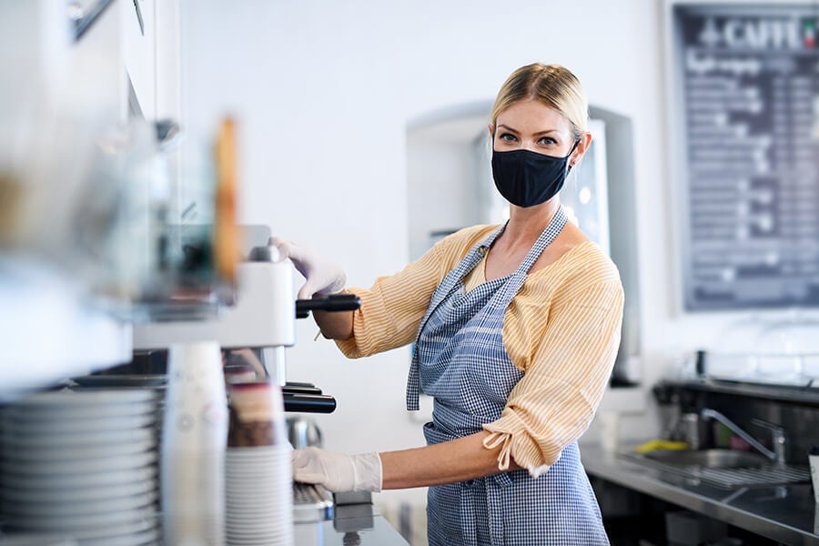 Young woman operating a coffee machine while using a quality-certified NEN-spec-1-2 face mask