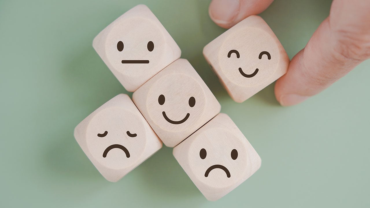 Fem tärningar som visar illustrationer av glada och ledsna ansikten i olika grader. 