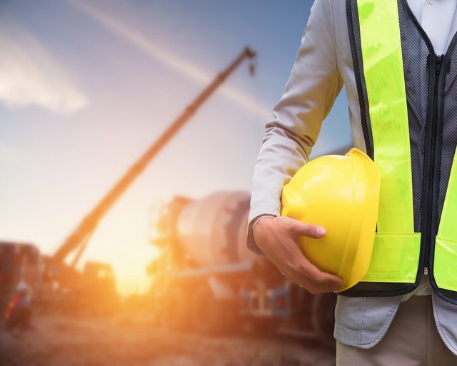 close-up of a man holding a helmet in a construction site during the golden hour