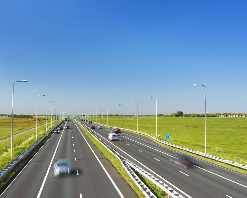 Snelweg met meerdere rijstroken in een open landschap onder een heldere blauwe hemel.