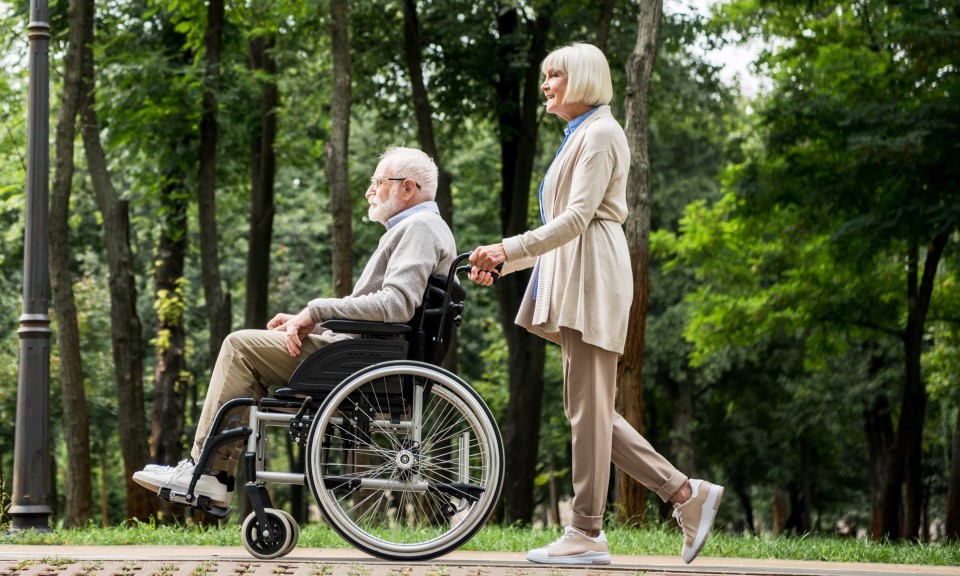 Oudere man in een rolstoel wordt voortgeduwd door een vrouw in een park