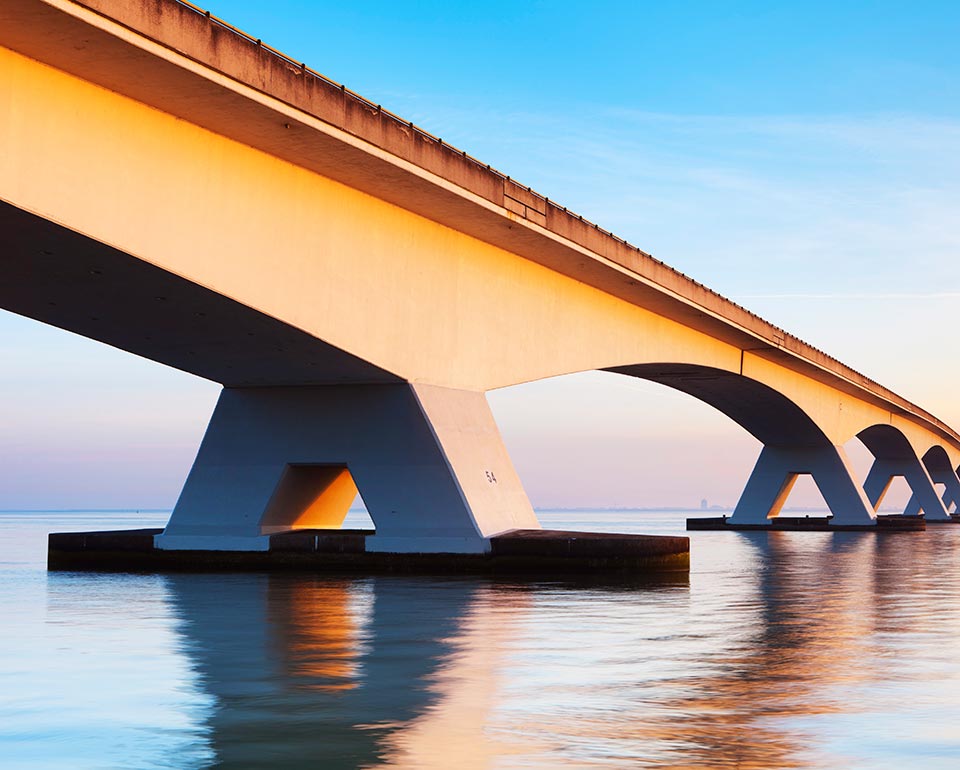 En lång modern bro av betong, över lugnt och stilla vatten.