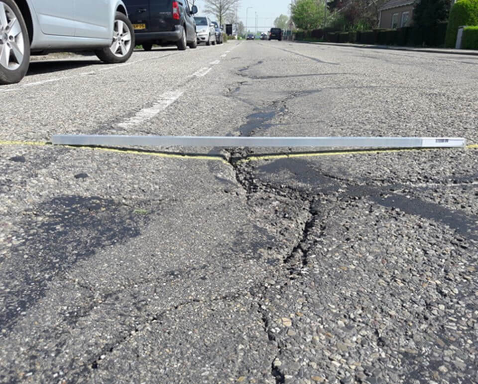 Een gebarsten asfaltweg met zichtbare scheuren en een meetinstrument dat over de scheuren is geplaatst