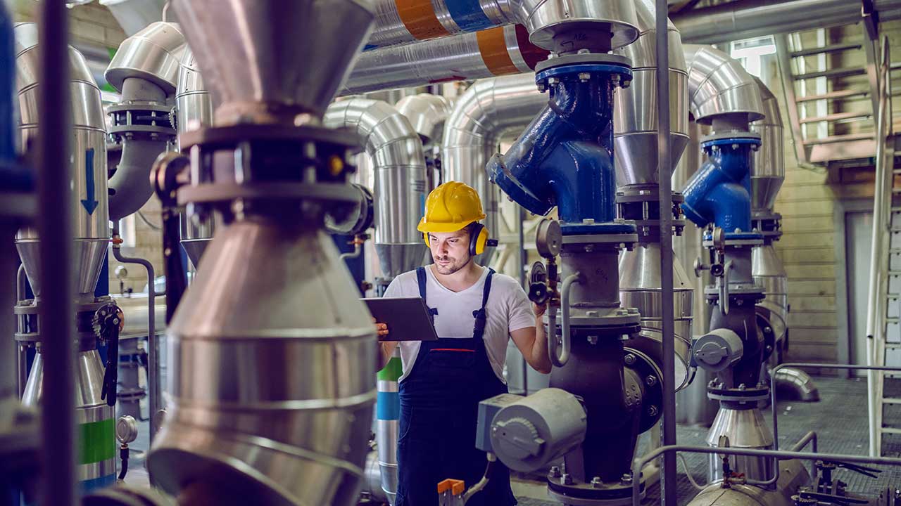 Pannoperatör med skyddshjälm justerar trycket för tryckkärl och läser instruktioner från en läsplatta.