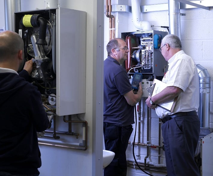 Kiwa instructor with student during training, discussing a heating system in a maintenance room, highlighting HVAC system repair and diagnostics